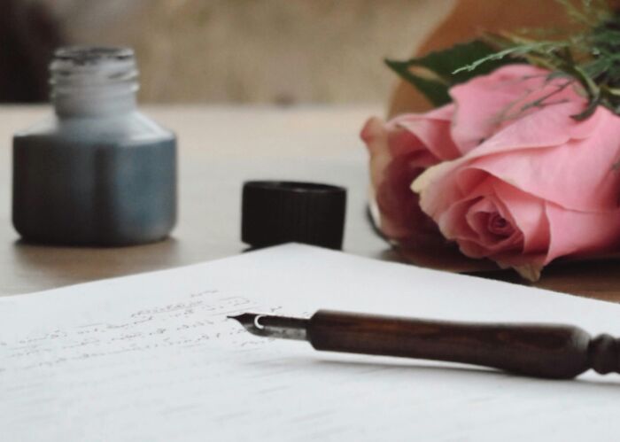 Fountain pen on paper beside ink bottle and pink roses, capturing eye-opening moments of writing.
