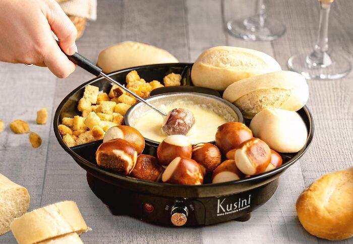 Hand dipping pretzel bite into cheese fondue with bread and croutons, perfect for skip the boring date night ideas.