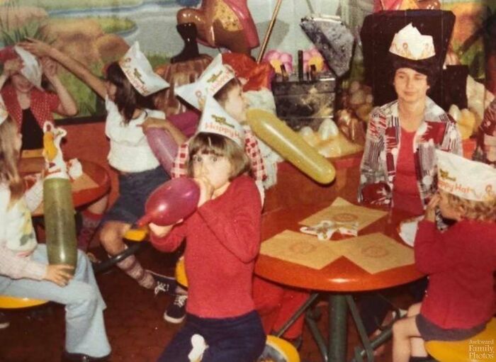 Children and adults wearing party hats and blowing up balloons in an awkward family photo with a sweet atmosphere.