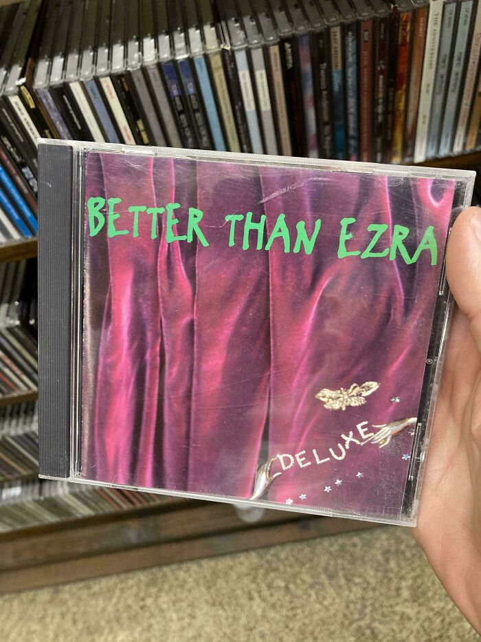 CD of Better Than Ezra's "Deluxe" album, featuring iconic '90s design, held in front of a shelf of music CDs.