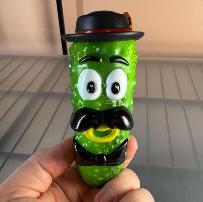 A green pickle with cartoon eyes and a mustache, topped with a black hat; an example of weird things that actually exist.