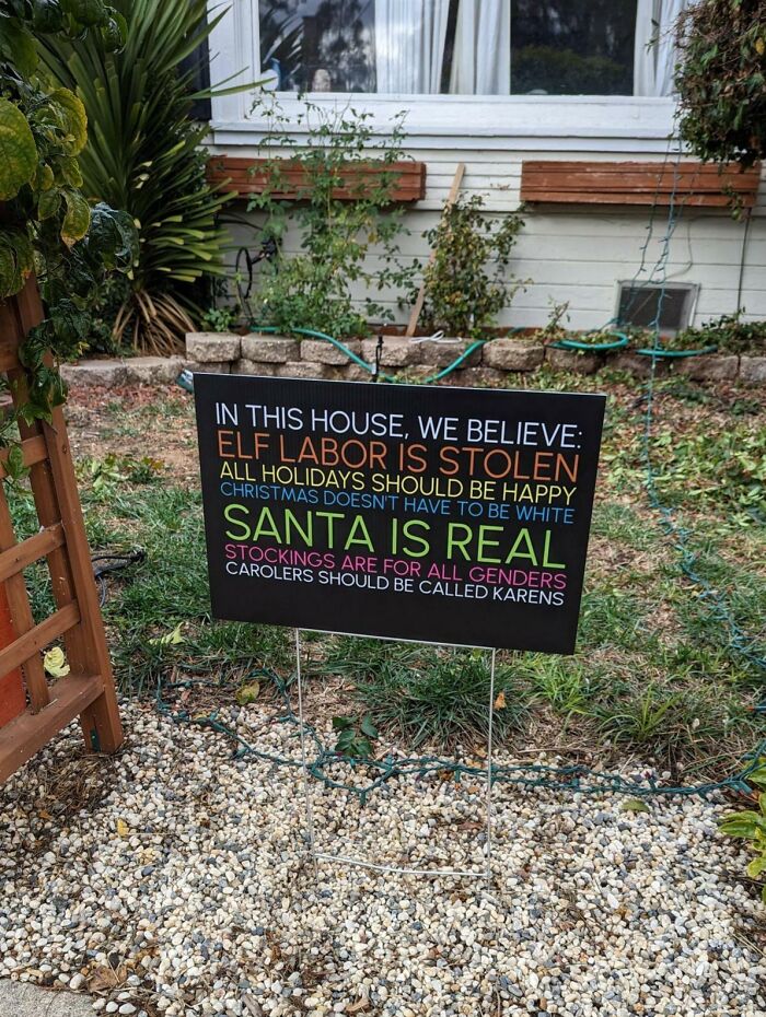 Funny sign in front yard with humorous statements about holiday beliefs.