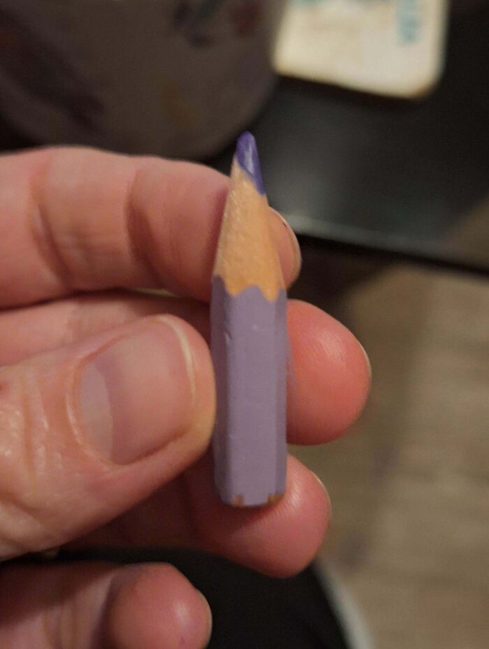 A small purple pencil held between fingers, symbolizing consumerism fatigue.