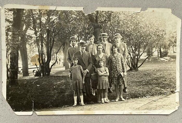 Vintage family photo in a park, linked to terrifying backstories, with adults in hats and children in dresses.