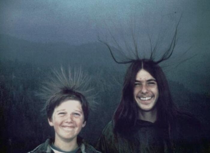 Two people with hair standing up in the foreground of a cloudy, eerie landscape. Photographs with terrifying backstories.