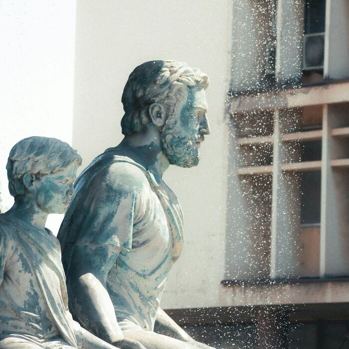 Statue of two figures side by side, weathered bronze texture, embodying mic-drop-moments in a serene urban setting.