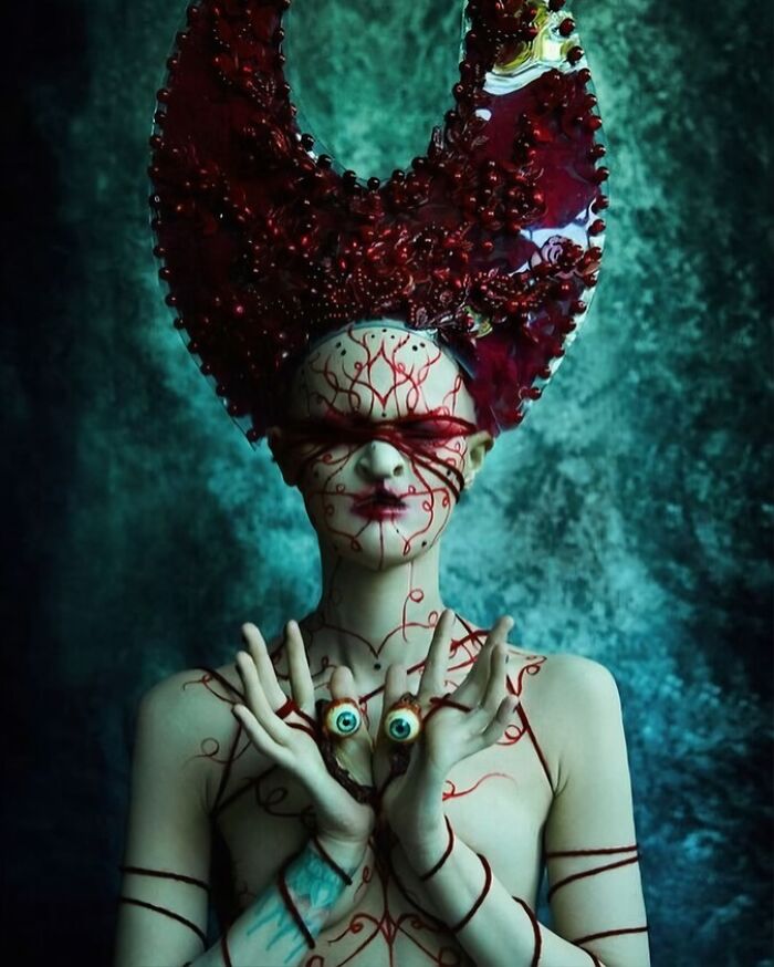 Unique model in an artistic headpiece and body art, posing with an expressive gesture against a textured background.