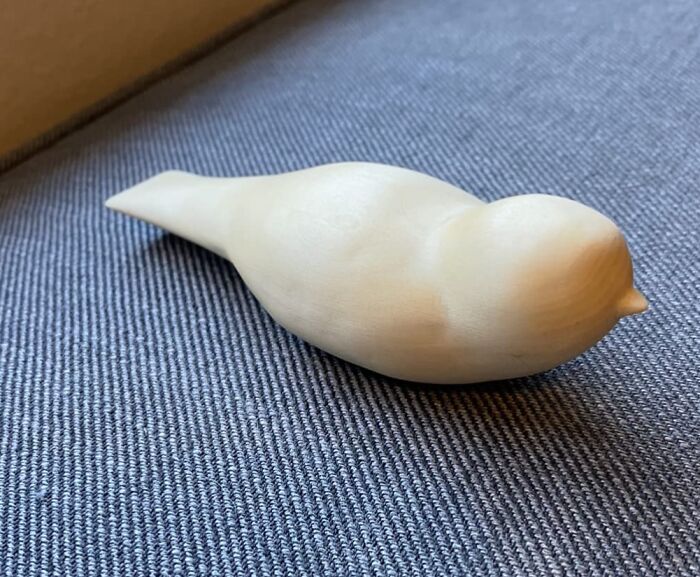 A wooden bird sculpture on a gray fabric surface, showcasing artistic design.