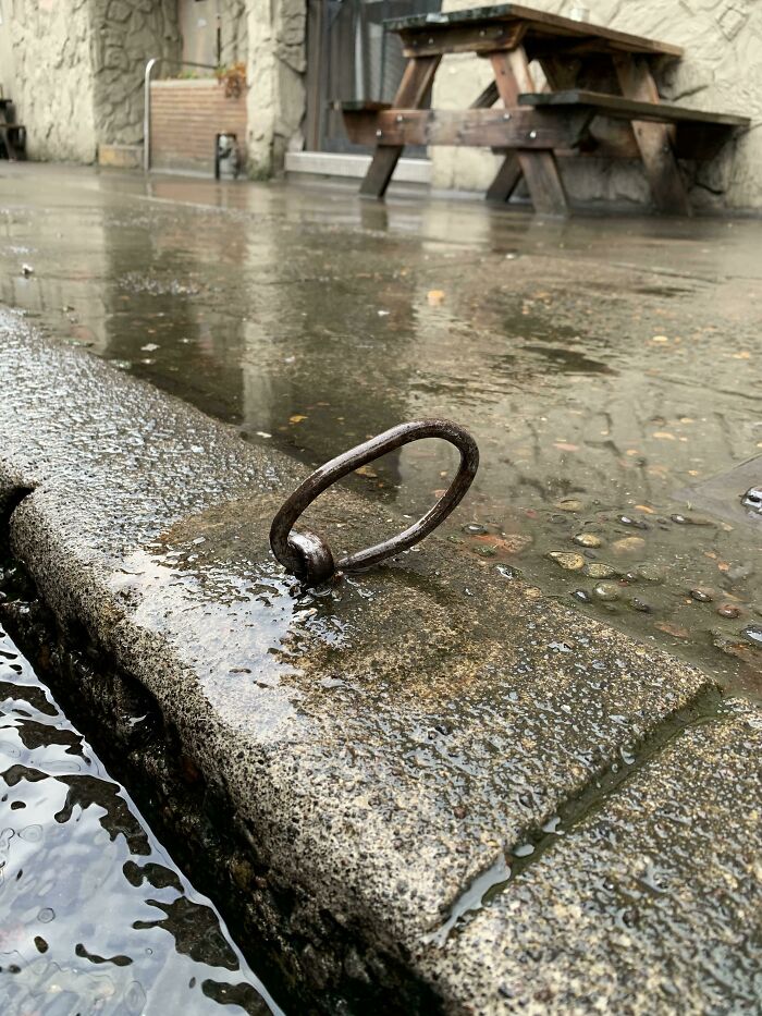 Rusty metal ring embedded in wet pavement as part of cities-genius-solutions for drainage.