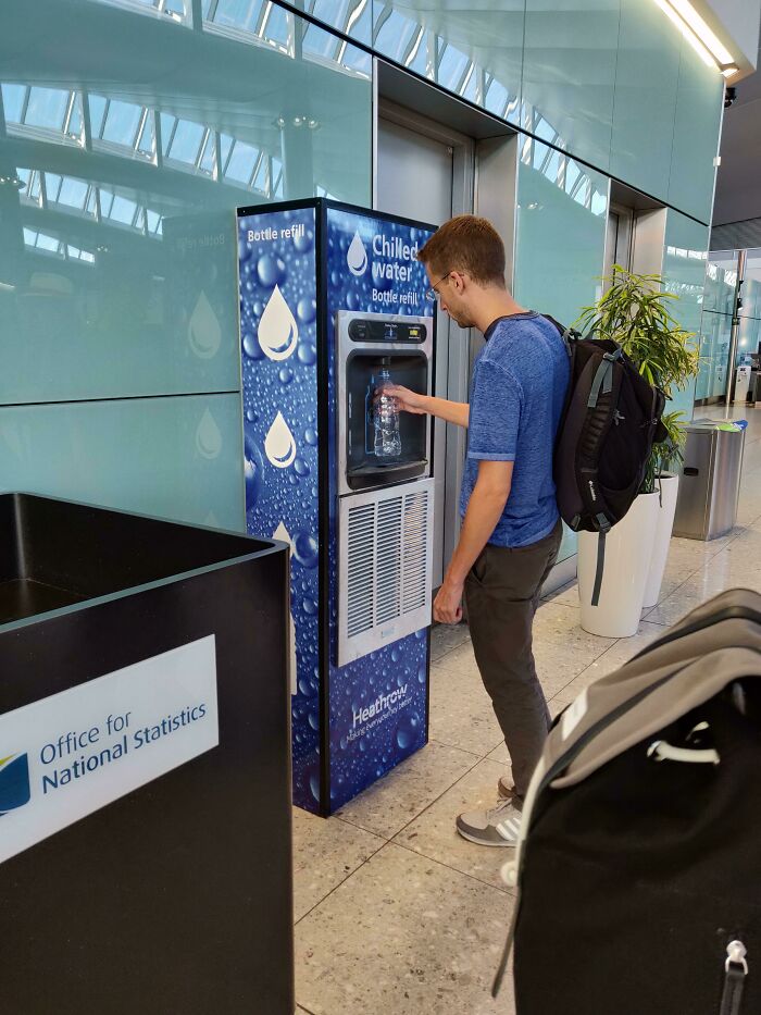 Person refilling water bottle at an airport water station, showcasing Cities-Genius-Solutions for sustainable travel.
