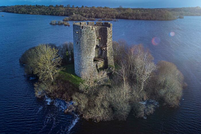 Ancient stone tower surrounded by water, with trees growing around and reclaiming the civilization structure.