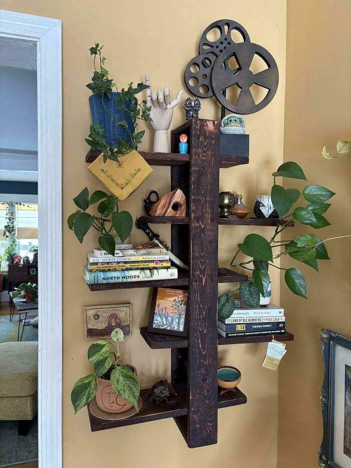 Dark wooden wall shelf with books, plants, and decorative items in a beautifully decorated home living space.