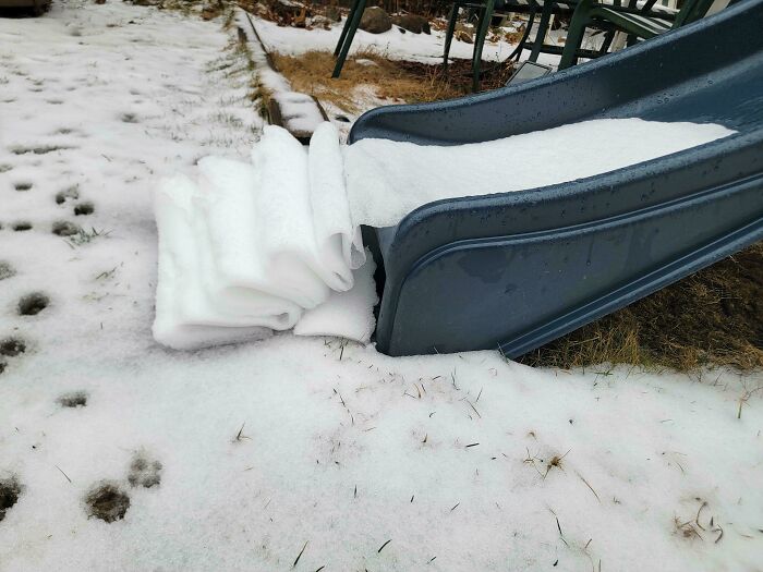 Snow peeled away from the edge of a slide in smooth layers, a moderately interesting sight shared outdoors in winter.