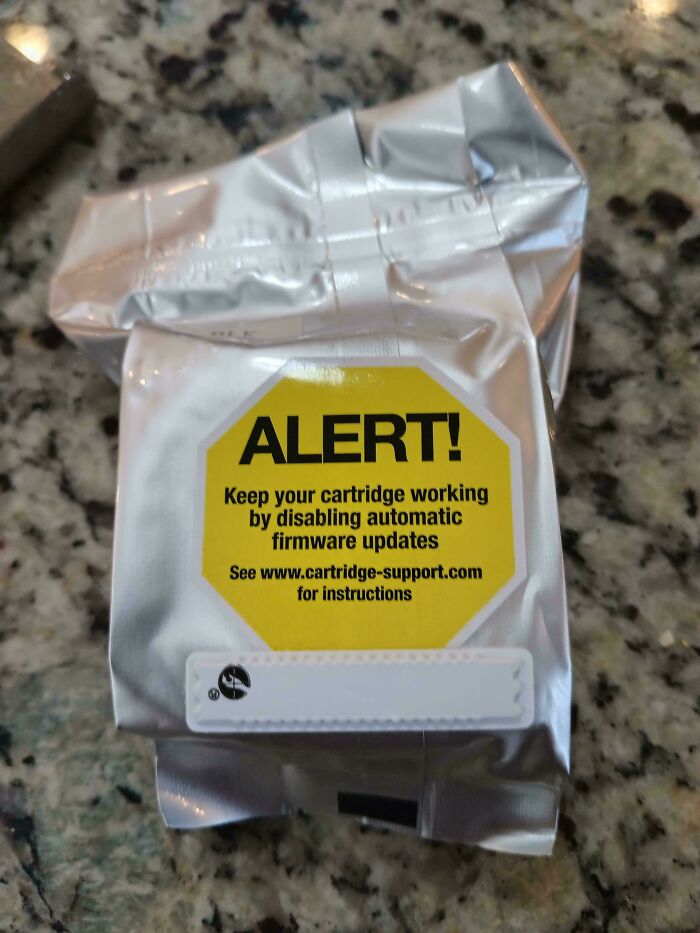 Silver cartridge packaging with a yellow alert label about disabling automatic firmware updates on a granite countertop