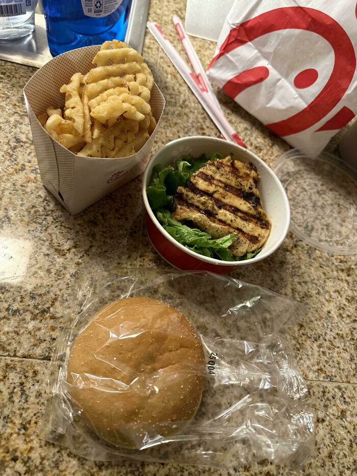 Fast food meal with waffle fries, grilled chicken on lettuce, and a sandwich bun seen as moderately interesting by people online.
