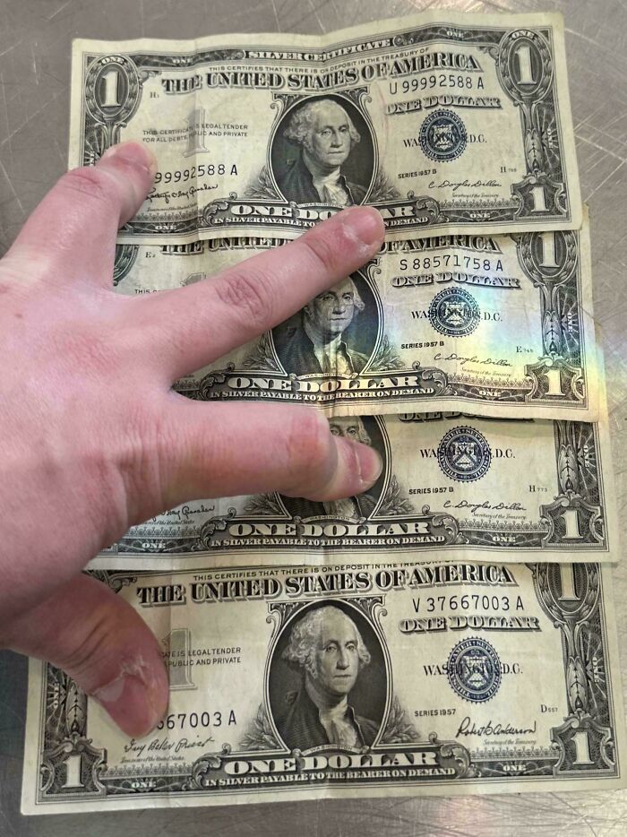 Hand holding four moderately interesting vintage silver certificate one dollar bills with different series years on metal surface.