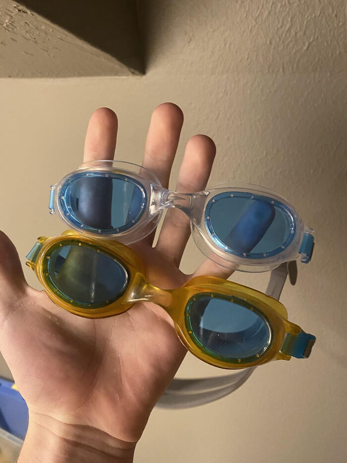 Hand holding two pairs of swim goggles with blue lenses, showing moderately interesting details in the design.