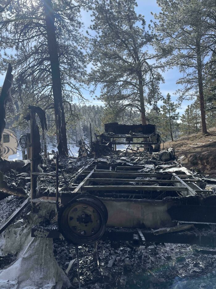 A charred vehicle frame, remnants of a severe accident, stands amidst burned trees, showcasing the aftermath of fails.