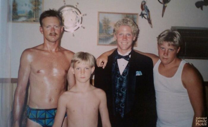 Awkward family photo showing a shirtless man with three boys, one dressed in a tuxedo, capturing a sweet moment.