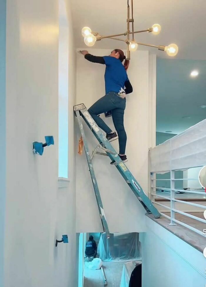Person balancing on an unsafe ladder setup over a stairway, creating a potential "death stairs" hazard.