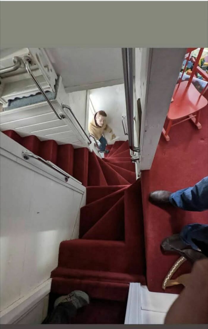 Narrow spiral staircase with red carpet and safety railings, viewed from above.