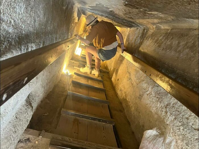 Person climbing steep narrow stairs with wooden steps, holding onto rails, illustrating challenging "death stairs" experience.