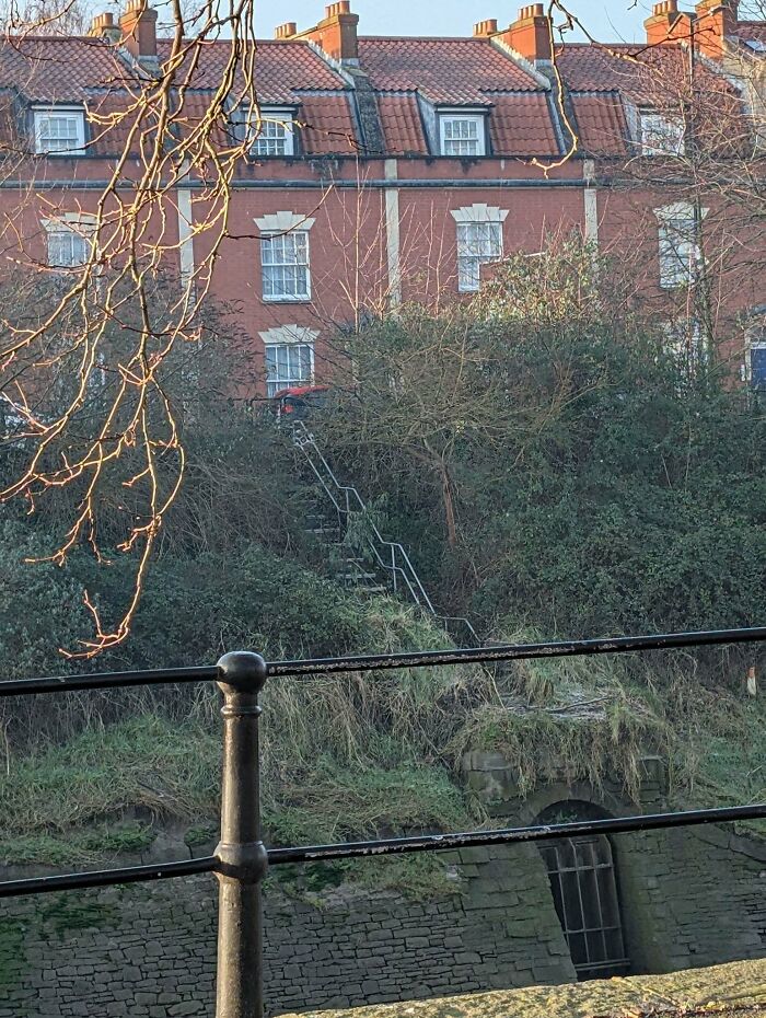 Steep stairs leading up to a brick building, surrounded by overgrown vegetation, resembling so-called "death stairs".