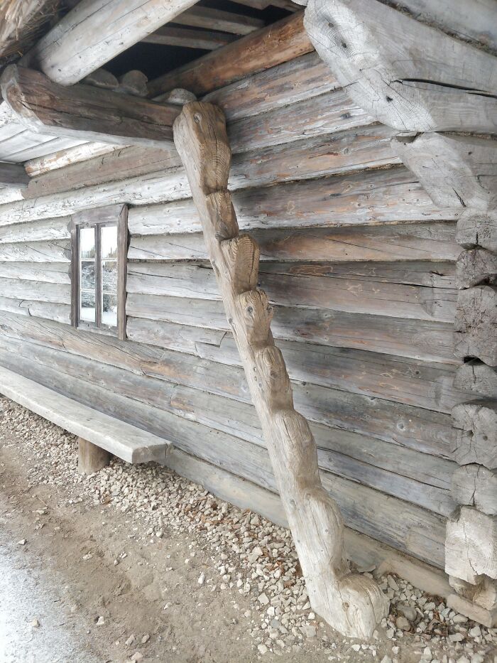 Rustic wooden "death stairs" leaning against a log cabin wall, surrounded by gravel.