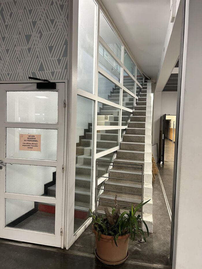 Staircase with sharp turns behind glass paneling, often called "death stairs," next to a door with a warning sign.