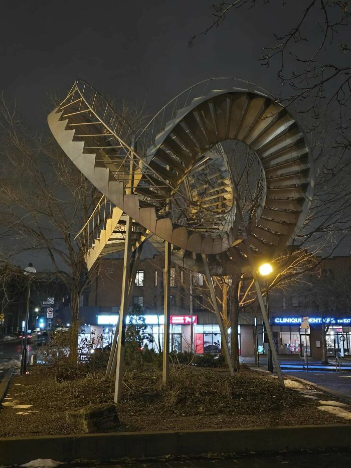Metallic spiral stairs in urban night setting, resembling artistic "death stairs" structure.
