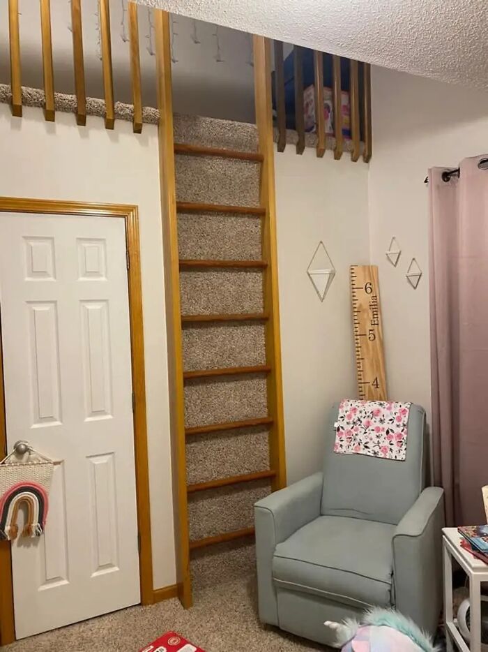 Narrow carpeted death stairs next to a white door in a cozy room with a light blue armchair.