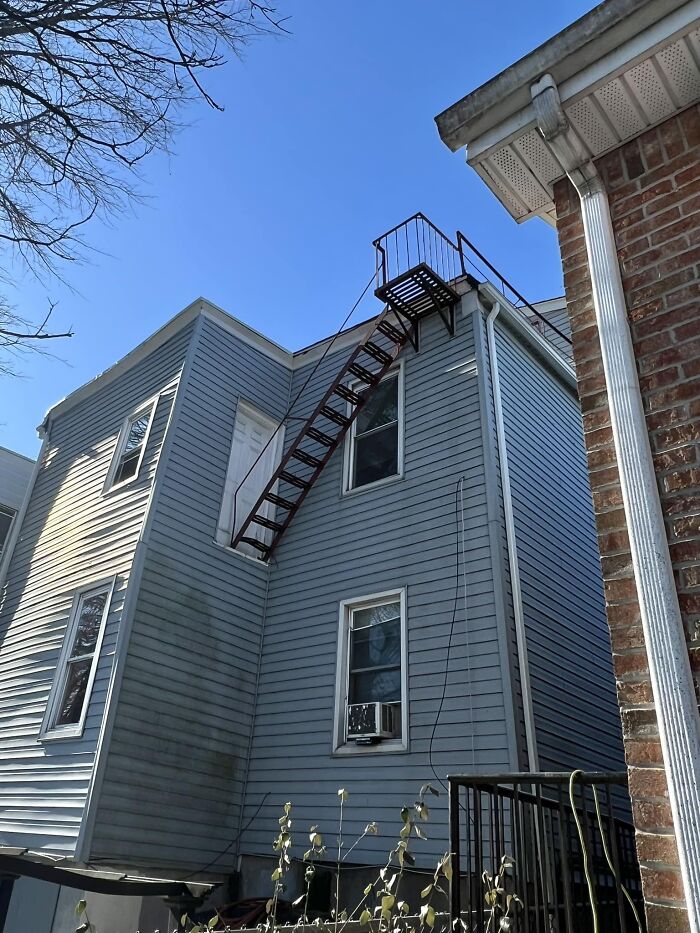 Unsafe exterior staircase on a building, known as "death stairs," with a steep ascent under a clear blue sky.