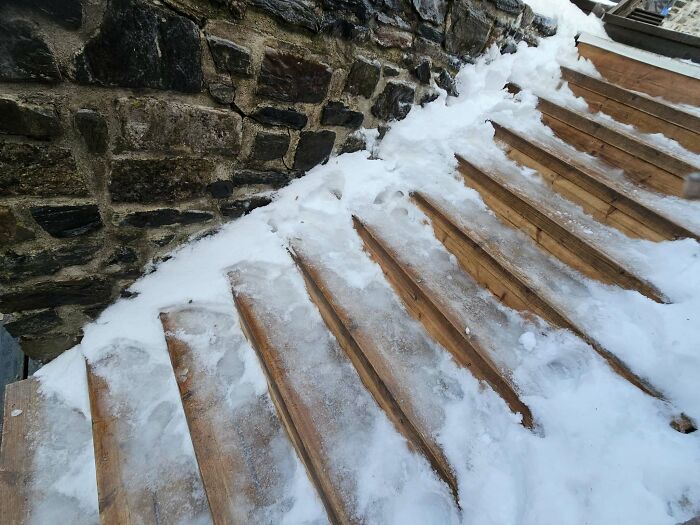 Icy wooden stairs next to a stone wall, resembling treacherous death stairs covered in snow.