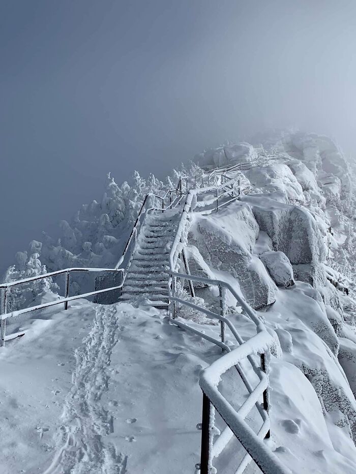 Snow-covered stairs on a treacherous mountain path under a foggy sky.