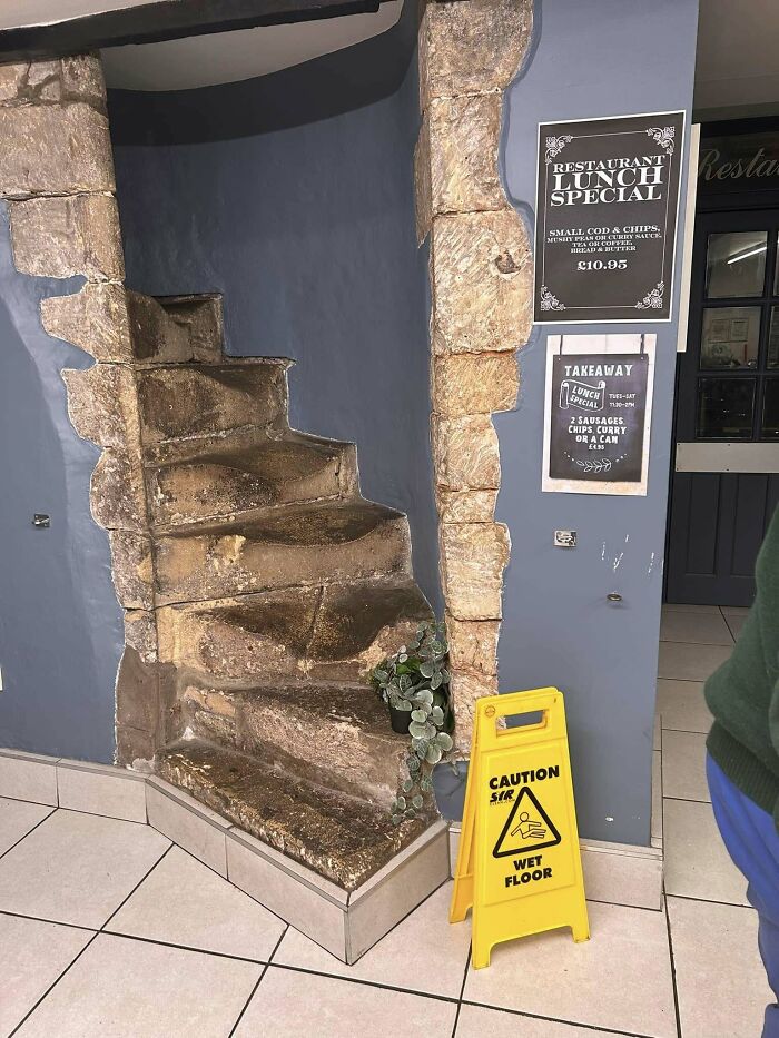 Rustic stone stairs in a restaurant with a caution sign placed nearby, suggesting potential danger.
