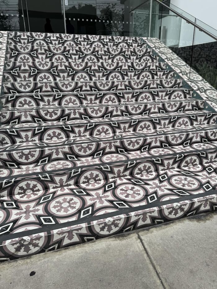 Intricately patterned death stairs with optical illusion effect, leading to a modern glass entrance.