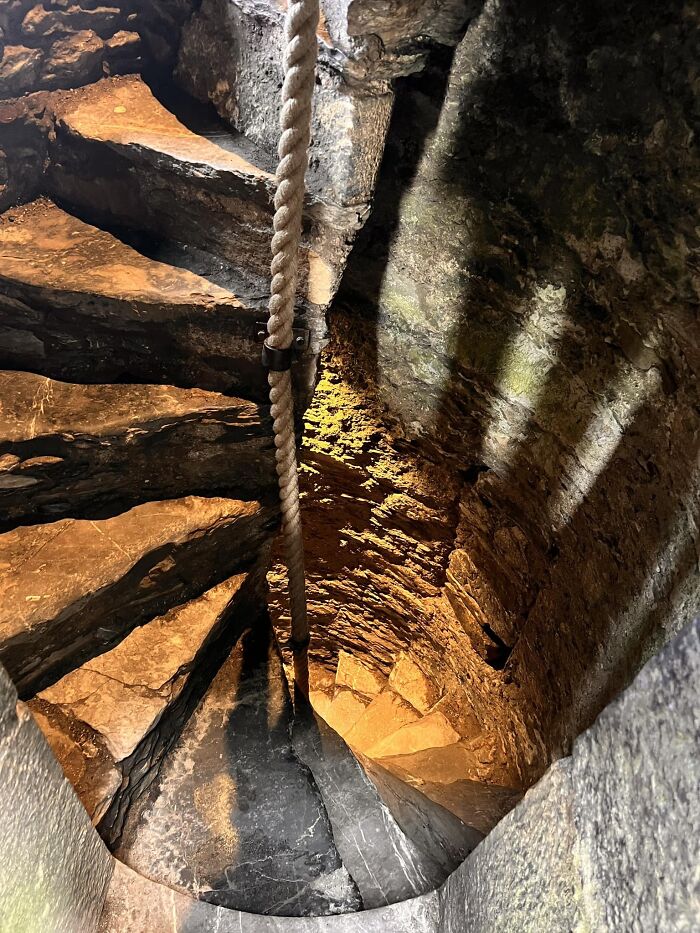 Spiral stone death stairs with a rope railing, dimly lit and enclosed by rough stone walls.