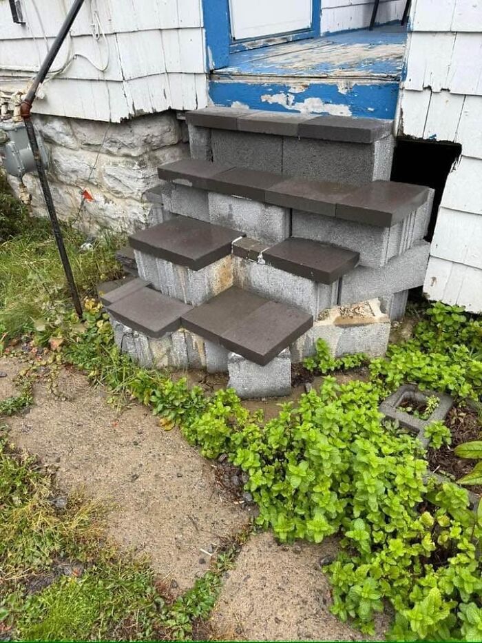 Crumbled stairs made of bricks leading to a worn-out porch, surrounded by grass, illustrating challenging "death stairs".