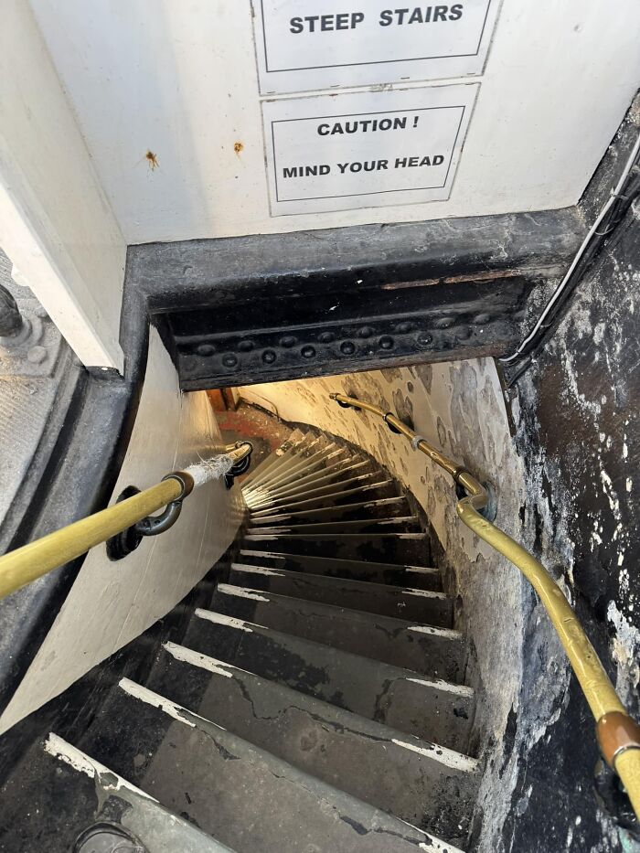 Narrow spiral stairway with warning signs about steep stairs and low head clearance.