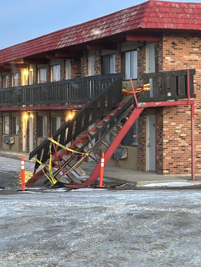 Damaged outdoor stairs with caution tape, highlighting safety concerns, beside a brick building.