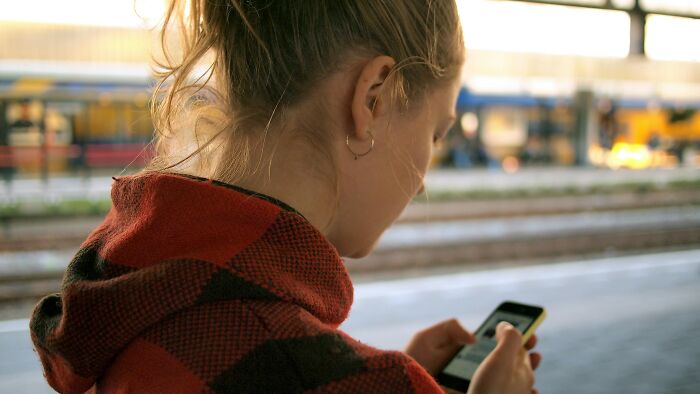 Woman in a checkered jacket looking at her phone at a train station.
