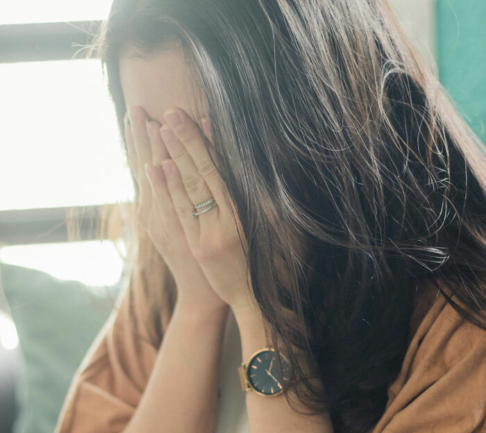 A woman covering her face in distress, wearing a watch and rings.