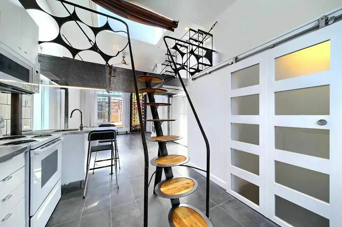 Modern kitchen showing "Death Stairs" with a unique, spiral design and wooden steps leading to a loft area.