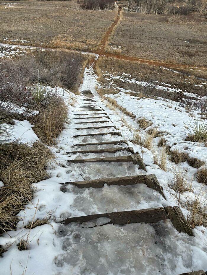 Snowy, uneven stairs on a hill, often called "death stairs," with a view of a dirt trail beyond.