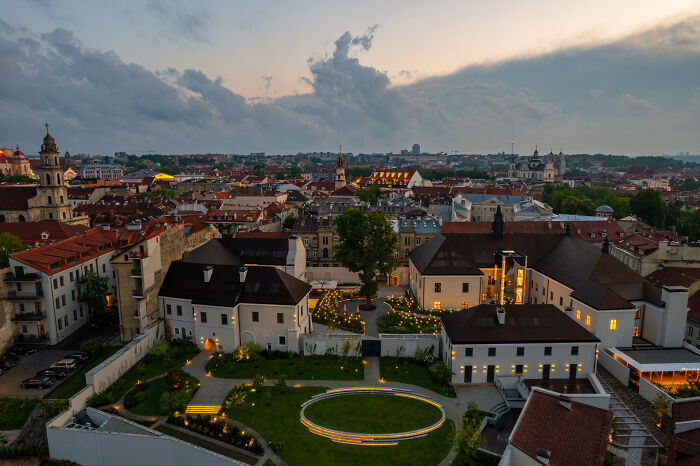 Aerial view of a Lithuanian cityscape at dusk, showcasing historic buildings and a lush courtyard.