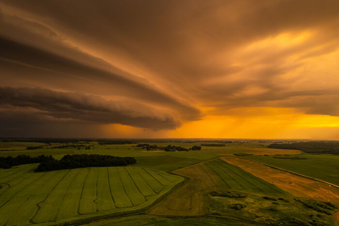 Aerial view of Lithuania's green fields under dramatic, golden-clouded sky at sunset.