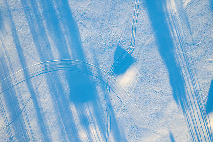 Aerial view of Lithuania's snowy landscape with long shadows and curved tracks.