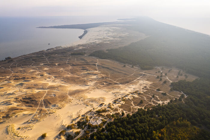 Aerial view of Lithuania's picturesque landscape featuring vast sandy dunes and sprawling forests.