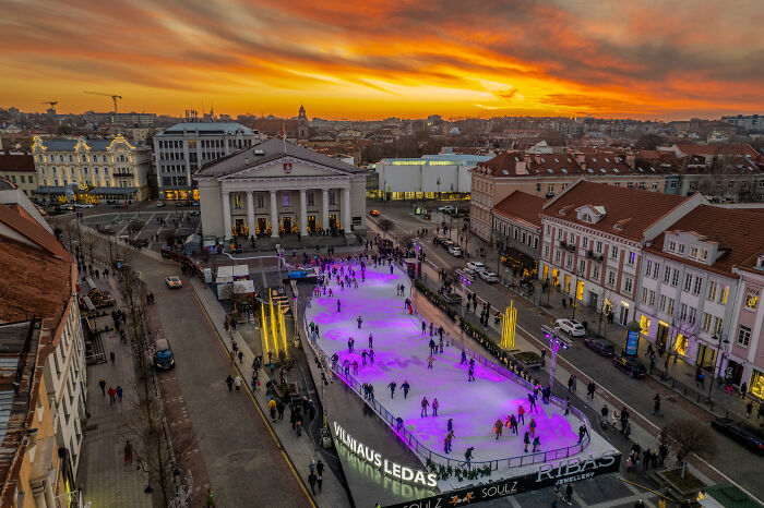 Bird’s-eye view of a vibrant skating rink in Vilnius, Lithuania, at sunset, surrounded by historic buildings.