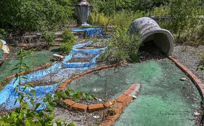 Overgrown mini-golf course as nature reclaims civilization, with plants and foliage covering structures.